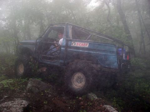 1988 Ford Bronco - A modified off-road vehicle navigates a muddy trail surrounded by dense trees and fog.