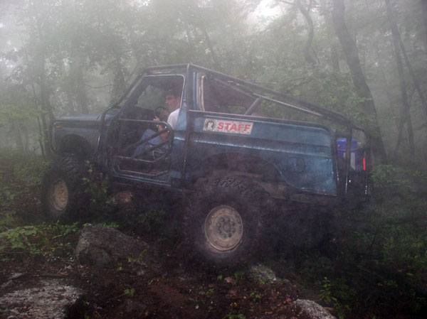 Off-road vehicle with a roll cage driving through a foggy forest. A person is in the driver's seat