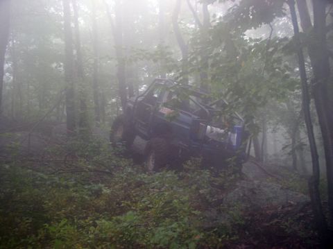 1988 Ford Bronco - A blue 1988 Ford Bronco navigates a steep, wooded trail on a foggy day.