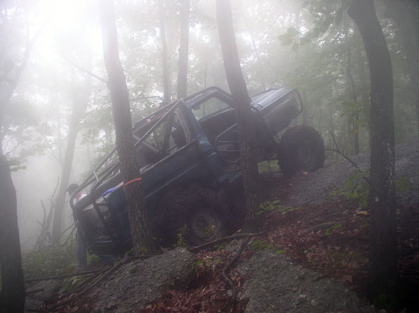 Off-road vehicle tilted on a foggy, wooded trail, with trees close on either side