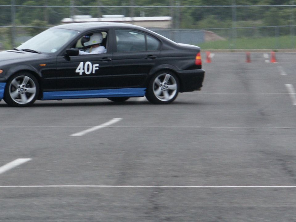 Black sedan with blue side skirts and white number '40F' on the door, seen from the side on a race track