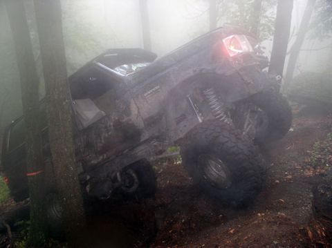 1988 Ford Bronco - Off-road vehicle stuck between trees in foggy woods, showing mud and suspension details.
