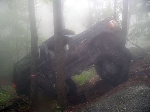 1988 Ford Bronco - A black SUV navigates a challenging off-road course on a foggy day, with trees obscuring the view.
