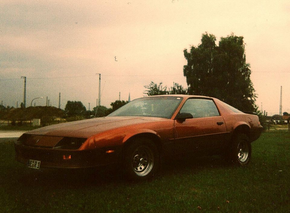 Brown 1980s Chevrolet Camaro coupe parked on grass at dusk