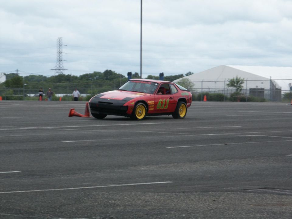 Red sports car with yellow wheels and number 611 on the door, on a paved track with orange cones