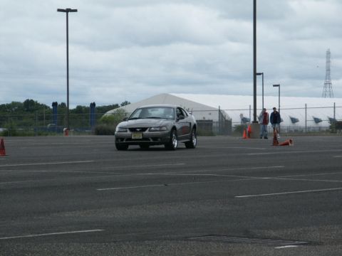 2001 Mercury Grand Marquis - A gray Ford Mustang is seen on a paved lot with traffic cones and two people in the background.