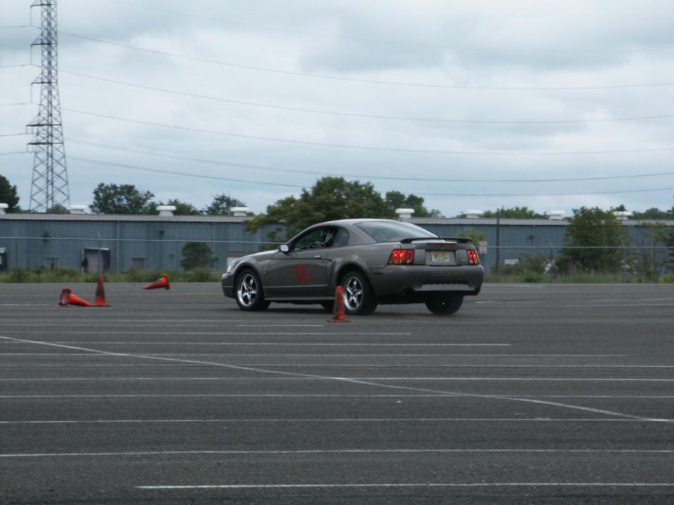 Gray Ford Mustang with red number 10 on door, driving on asphalt course with orange cones
