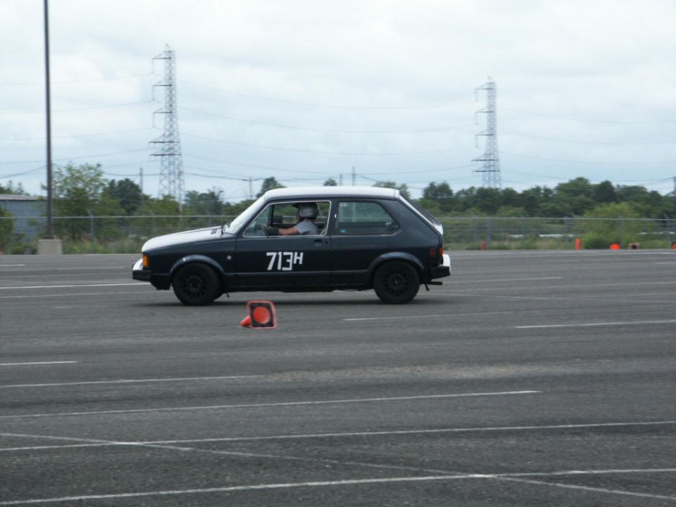 Black hatchback with white roof and '713H' on the side, driving on a track with orange cones