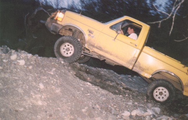 Yellow Ford F-Series 4x4 pickup climbing a rocky embankment at dusk