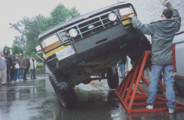 Lifted Ford truck flexing one wheel up a red steel ramp at a wet outdoor event