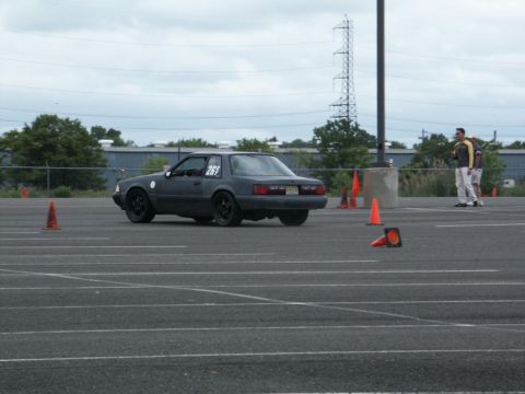 2001 Mercury Grand Marquis - A dark gray coupe with racing numbers is seen on a track, navigating around orange cones.