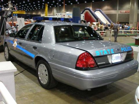 1998 Ford Crown Victoria - Silver Ford Crown Victoria police sedan shown from the rear three-quarter angle, marked 'STATE POLICE' in blue lettering with a blue and wh…
