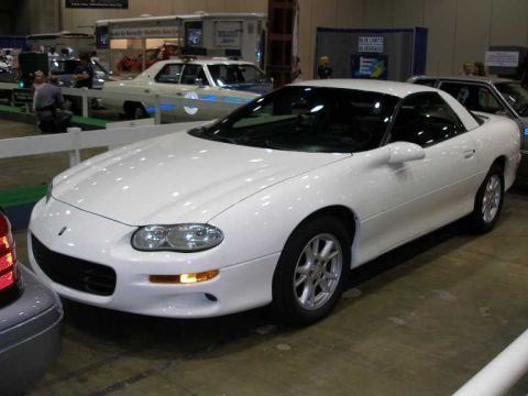 1998 Ford Crown Victoria - A white fourth-generation Chevrolet Camaro coupe shown from the front three-quarter angle at an indoor auto show, with one amber front turn…