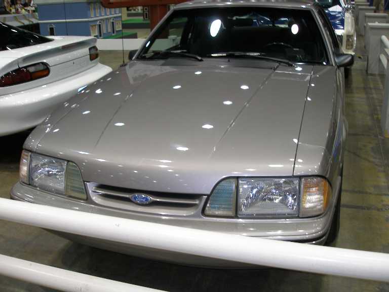 Front of silver Fox-body Ford Mustang behind white barrier indoors
