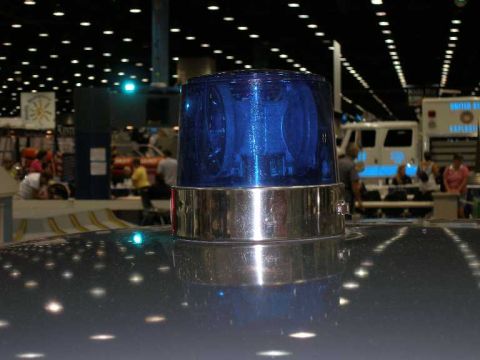 1998 Ford Crown Victoria - Close-up of a vintage blue rotating beacon with a chrome base mounted on a car roof inside a large convention hall. Show booths, spectators…
