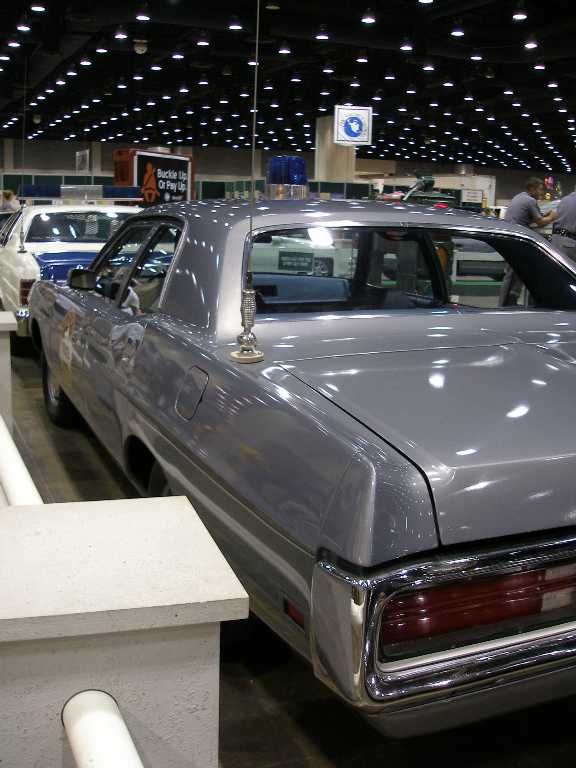 Silver 1970s four-door sedan rear view with whip antenna at indoor car show