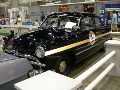 1998 Ford Crown Victoria - Three-quarter front view of a restored black late-1940s Ford 'shoebox' sedan in Kentucky State Police livery, with a gold side stripe, roun…