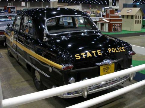 1998 Ford Crown Victoria - A black late-1940s Ford sedan restored as a Kentucky State Police cruiser, with gold 'STATE POLICE' lettering across the trunk, a gold door…
