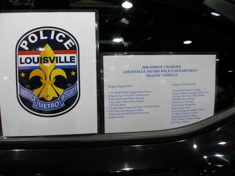 1998 Ford Crown Victoria - Two printed placards displayed on the black door/body of a dark vehicle: a Louisville Metro Police shield/logo and an information sheet tit…