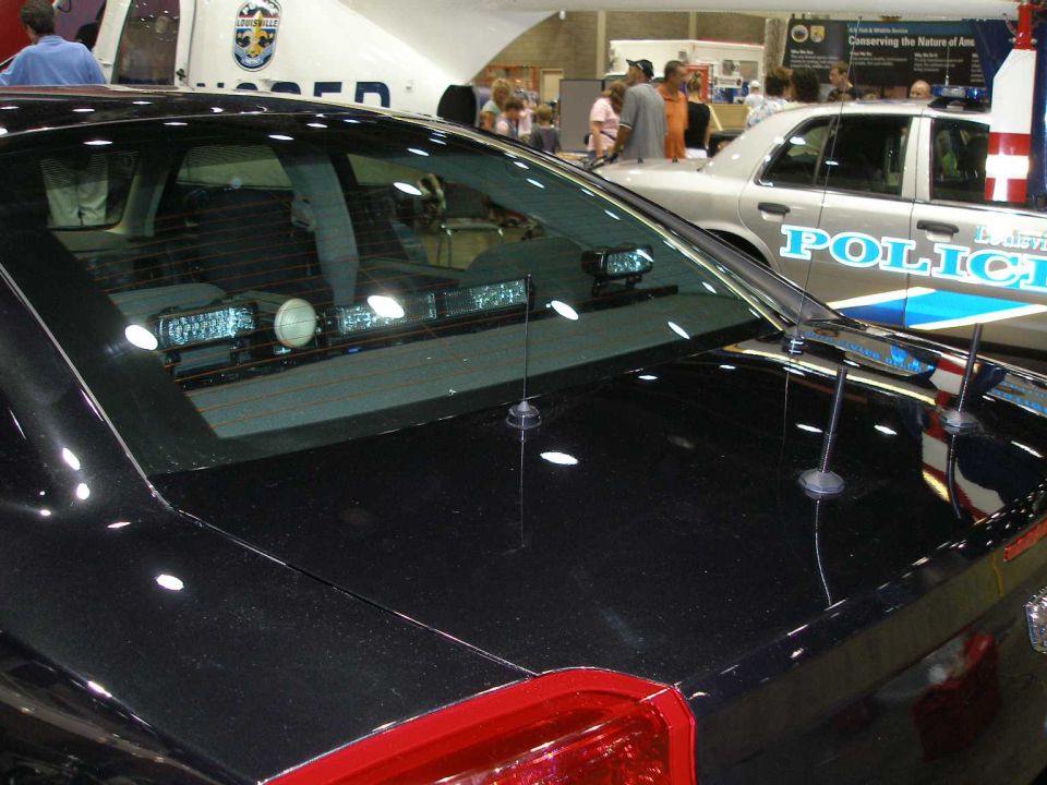 Black police sedan rear deck with interior light bar; white LMPD Crown Victoria behind.