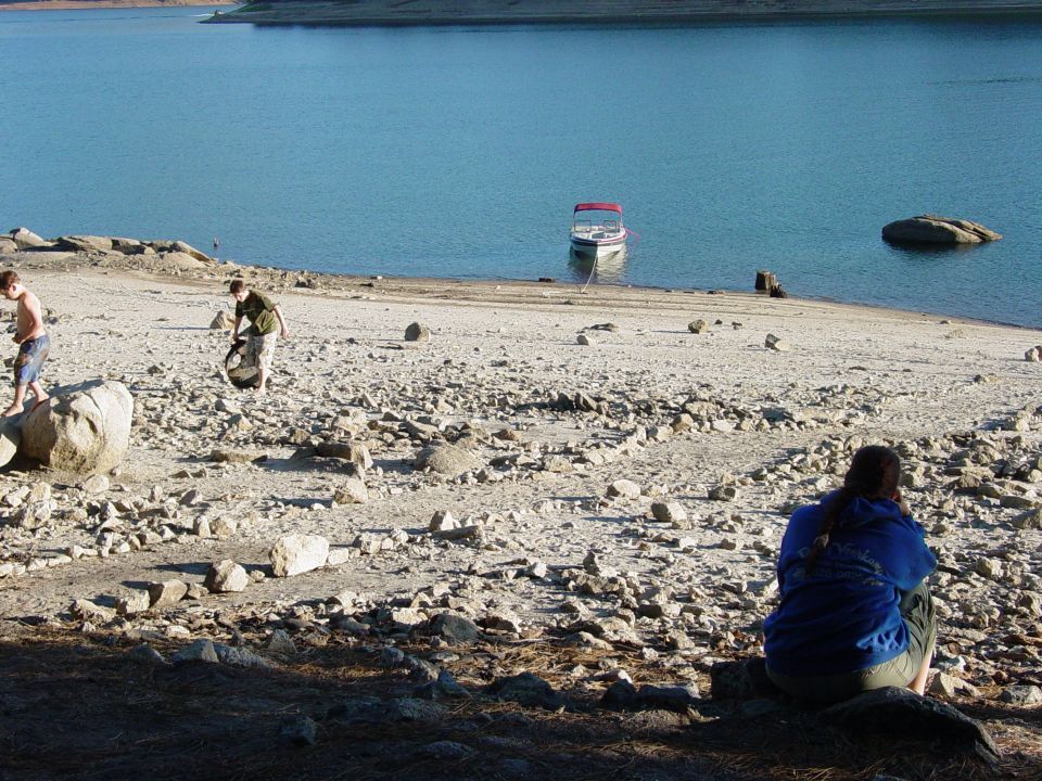 Boat tied to shore on a rocky beach with people nearby
