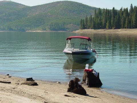 1986 Ford Bronco - A boat with a red canopy rests on calm lake waters, with a wooded shoreline and hills in the distance.