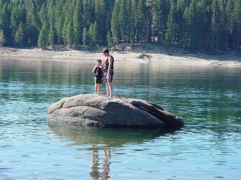 1986 Ford Bronco - Two people stand on a rock in a lake, with a forest and dry shore visible.