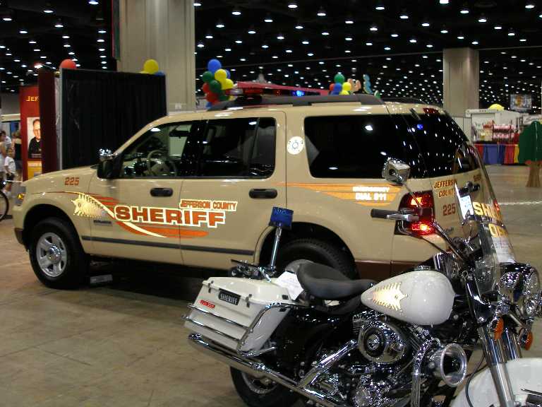 Tan Jefferson County Sheriff SUV and white police motorcycle at indoor show