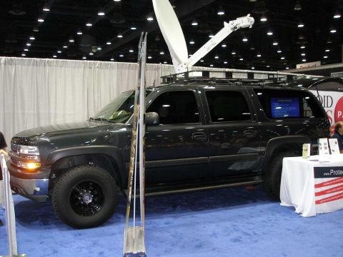 1998 Ford Crown Victoria - A black full-size Chevrolet Suburban SUV shown in side/3q-front profile at an indoor trade show, fitted with a roof rack and a large white…