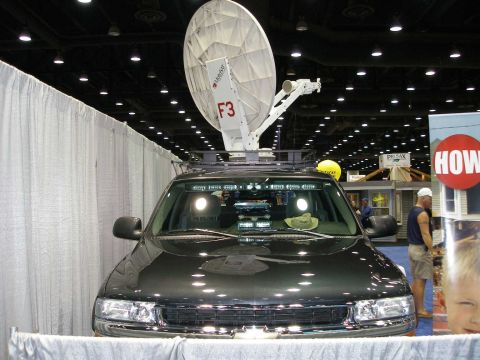 1998 Ford Crown Victoria - Front view of a dark green/black Chevrolet SUV displayed indoors at a trade show, fitted with a roof-mounted white satellite dish antenna l…