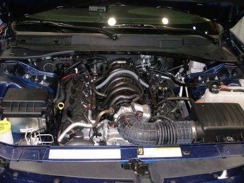 1998 Ford Crown Victoria - Engine bay of a dark blue vehicle, showing a V-configuration engine with a black plastic intake manifold, curved rubber air intake tube, an…