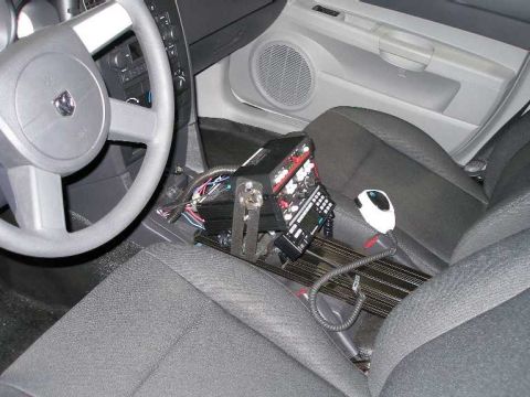 1998 Ford Crown Victoria - Interior view of a car with gray steering wheel and dark cloth bucket seats, showing a center console setup with police-type equipment: a m…