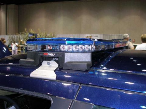 1998 Ford Crown Victoria - Close-up of a low-profile Code 3 LED emergency light bar with clear lenses mounted on the roof of a dark blue metallic vehicle, displayed i…