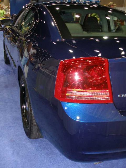 1998 Ford Crown Victoria - Rear three-quarter close-up of a dark blue Dodge Charger sedan, showing the driver-side taillight with red and clear lenses, rear quarter p…