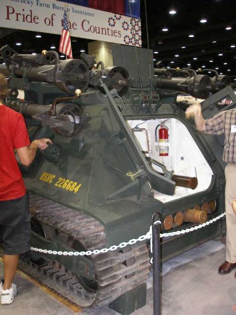 1998 Ford Crown Victoria - Rear quarter view of an olive-drab tracked armored personnel carrier displayed indoors at a convention center, marked 'USMC 226684' in yell…