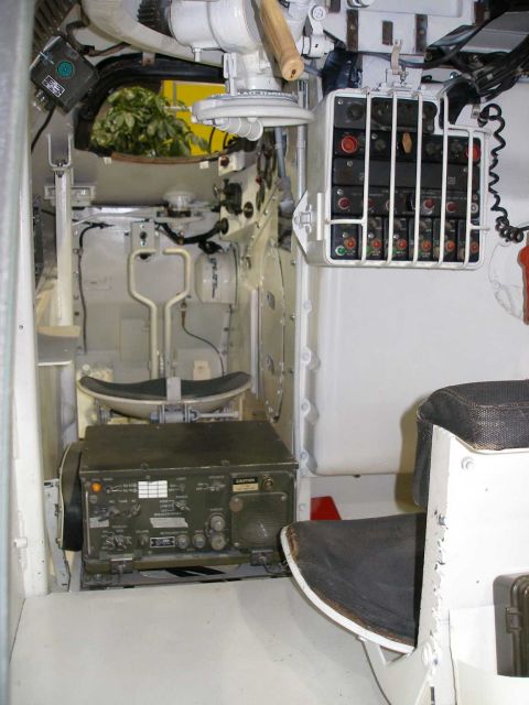 1998 Ford Crown Victoria - Cramped white-painted crew compartment of an armored military vehicle, with a green olive-drab field radio set mounted low, a caged electri…