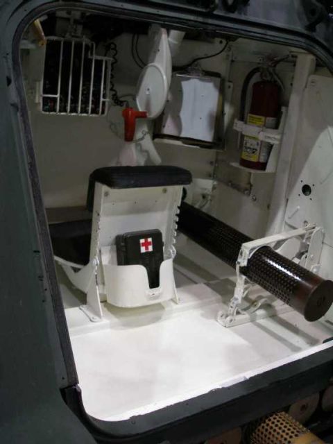 1998 Ford Crown Victoria - Interior of an armored military vehicle viewed through the rear hatch opening, showing the white-painted crew compartment with a padded sea…