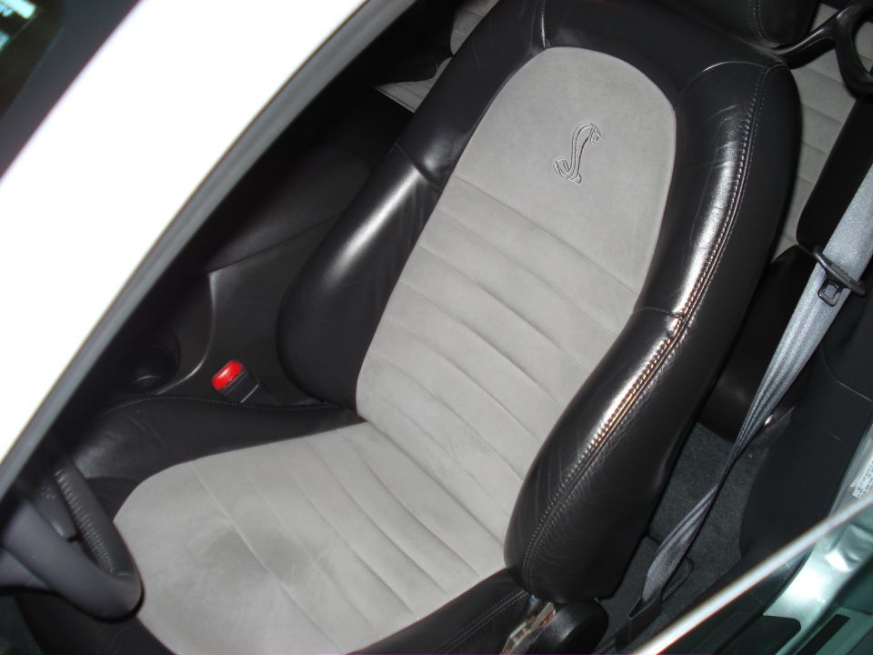 Car interior showing black leather and grey suede seats with a Cobra emblem stitched on the passenger seat