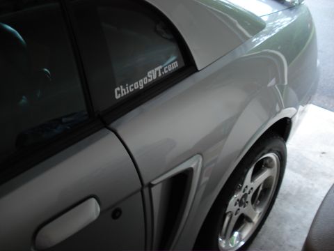 1998 Ford Taurus - A silver car is viewed from the side, revealing a distinctive vent and a website sticker on the rear window.