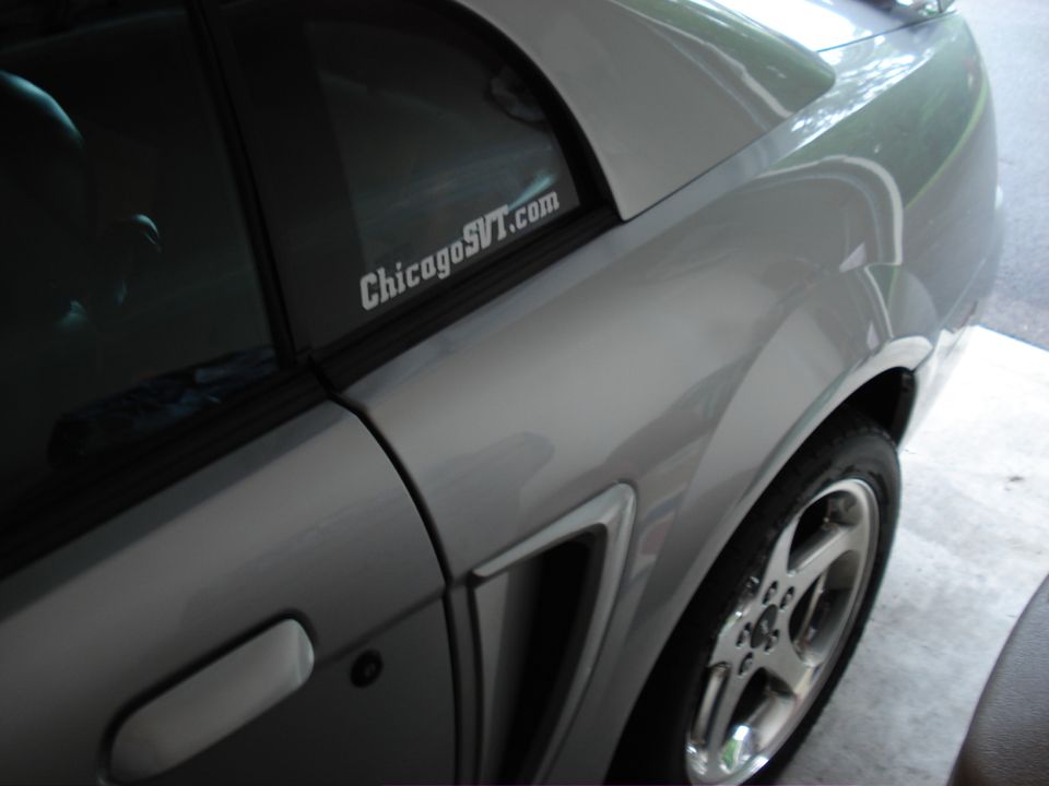 Silver car side view, showing a vent and a sticker on the rear window that says "ChicagoSVT.com"