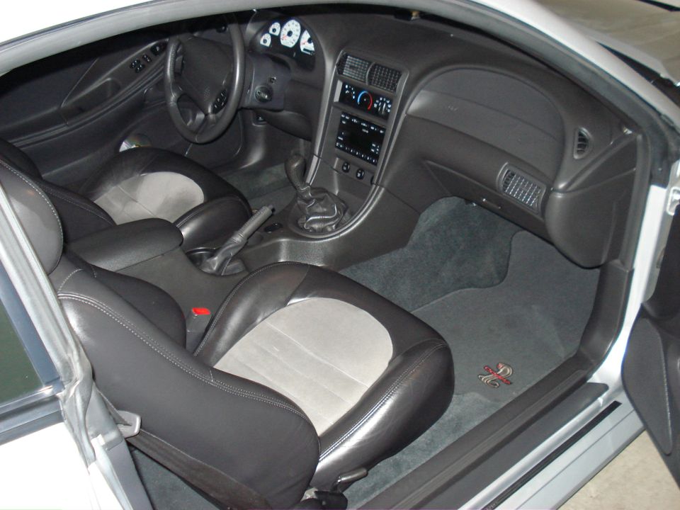 Interior view of a car with black and grey seats, dashboard, and floor mats with a red emblem