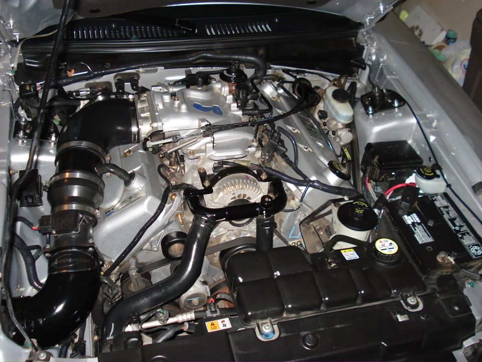 Engine bay with silver intake manifold, black hoses, and battery