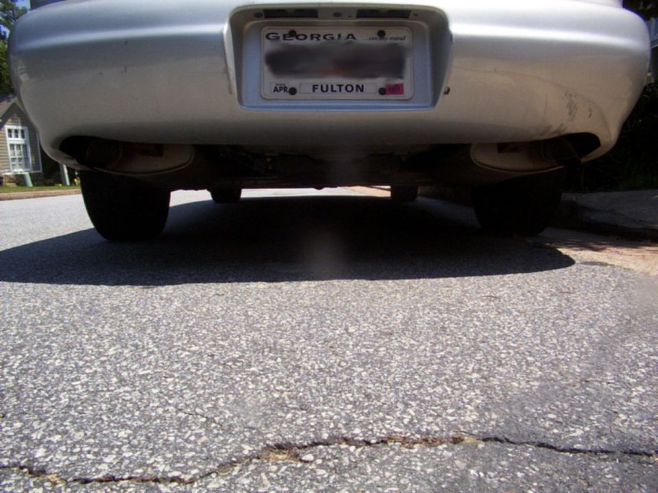 Rear bumper of silver sedan with Georgia Fulton plate, dual exhaust and visible exhaust vapor, low angle