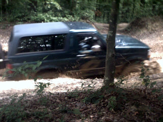 Dark green Ford Bronco driving through mud on a wooded trail