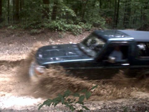 1996 Ford Bronco - A 1996 Ford Bronco navigates a muddy trail, kicking up dirt and water.