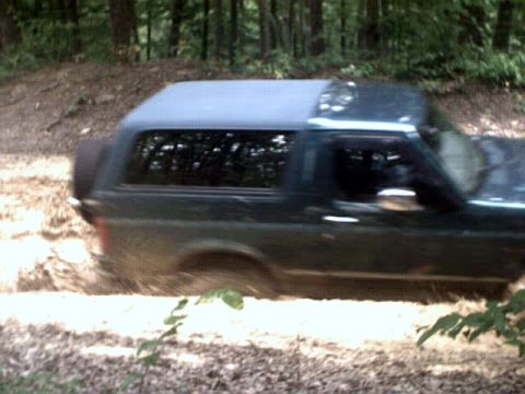 1996 Ford Bronco - Ford Bronco navigating a muddy off-road path surrounded by trees.