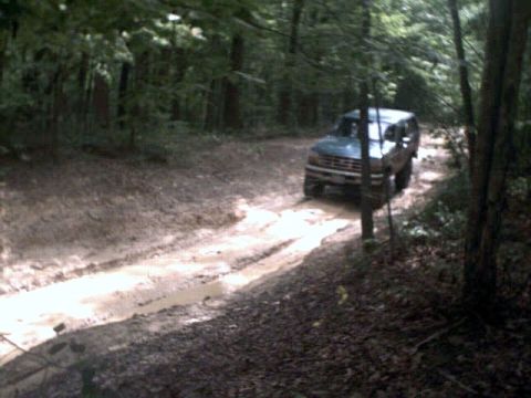 1996 Ford Bronco - A Ford Bronco navigates a challenging muddy path through a dense forest.