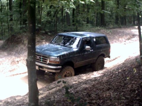 1996 Ford Bronco - A dark green 1992 Ford Bronco navigates a muddy off-road trail.