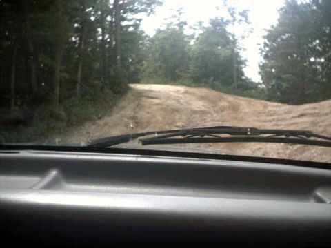 1996 Ford Bronco - View from inside a vehicle driving on a rough dirt road through a wooded area.