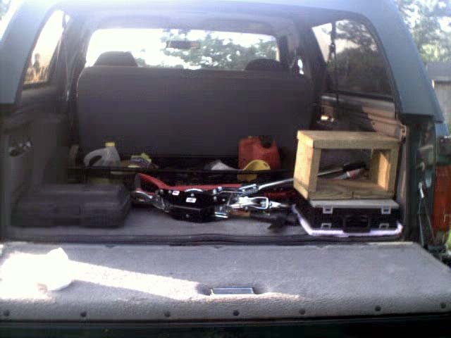 Interior cargo area of a dark SUV with tools, a plastic jug, and a wooden box
